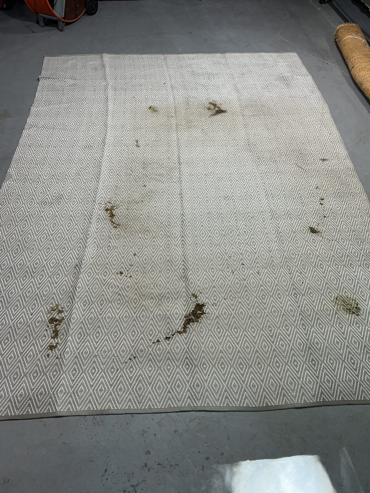 Taupe and ivory diamond flatweave rug covered in dark brown stains before cleaning
